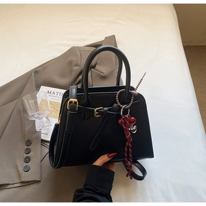 Detail of matte black tote bag with decorative buckle and red woven heart pendant accessory