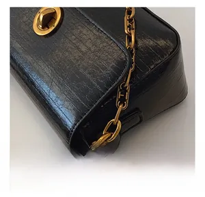 Close-up of black cracked texture leather shoulder bag with gold chain and twist lock