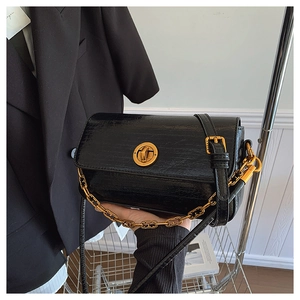 Detail of black glossy small square bag with golden ring lock and chunky chain