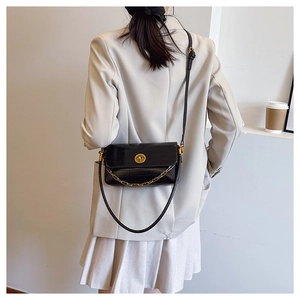 Detail of black glossy leather bag with gold chain and turn-lock worn by a model