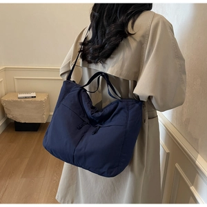 Détail du grand sac cabas bleu marine porté à l'épaule dans un décor minimaliste