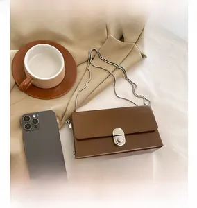 Detail view showing small dark brown glossy leather bag size compared to a smartphone