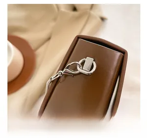 Detail of silver metal lobster clasp and snake chain on brown leather shoulder bag