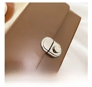Close-up of a silver metal lock buckle on a smooth dark brown leather shoulder bag