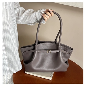 Detail of grey pleated leather tote bag with gold buckle on wooden table setting