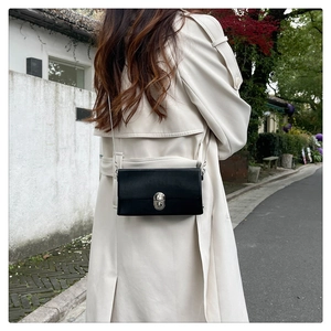 Detail view of a black leather rectangular crossbody bag with silver chain strap on model