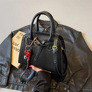Black pebbled leather tote bag with bow accent and heart charms on a leather jacket