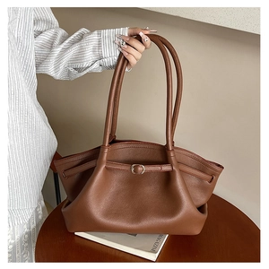 Detail of brown lychee grain leather tote bag with gold buckle on a wooden table
