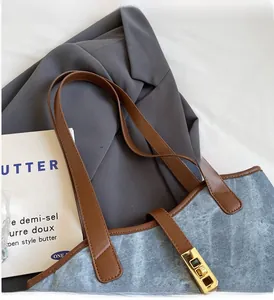 Détail du sac cabas en denim bleu clair avec anses en cuir marron et fermoir doré rotatif