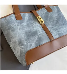 Détail du cabas en denim gris avec surpiqûres en cuir marron et fermoir doré