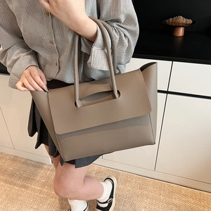 Detail of taupe pebbled leather tote bag shown on a model in a cozy lifestyle setting