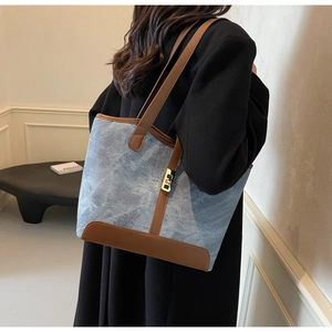 Détail du sac cabas en denim bleu avec bordure en cuir marron et boucle en métal doré