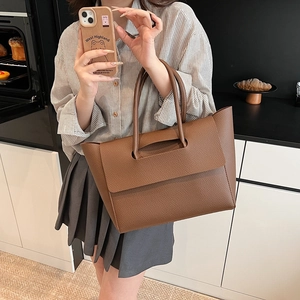 Detail of a brown lychee pattern leather tote bag held by a model in a kitchen setting