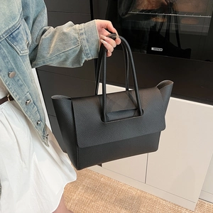 Detail of black pebbled leather tote bag with unique flap closure and integrated handle