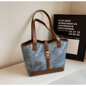 Détail du sac cabas en denim bleu avec garniture en cuir marron et boucle de verrouillage dorée