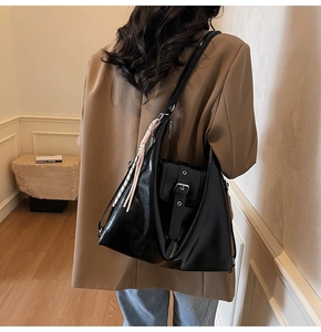 Détail du sac hobo en cuir noir avec boucle métallique et breloque en nœud tressé