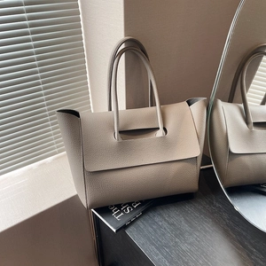 Close-up of a taupe grained leather tote bag with unique flap handles on a wooden table