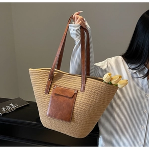 Close-up of woven straw tote bag with brown leather pocket and metallic rivet detail