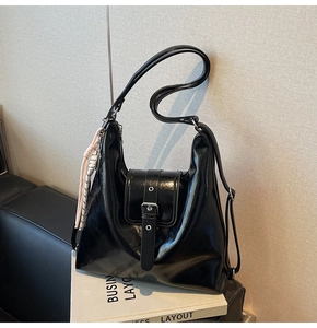 Détail d'un sac bandoulière noir brillant avec boucle argentée et breloque rose