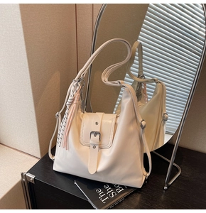 Détail du sac hobo crème avec breloque tissée et bandoulière réglable sur surface noire