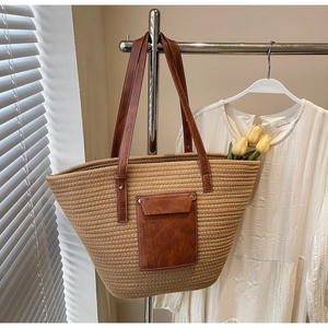 Detail of woven straw tote bag featuring brown leather shoulder straps and front flap pocket