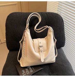 Détail du sac à bandoulière crème avec pompon tressé et boucle argentée sur une chaise