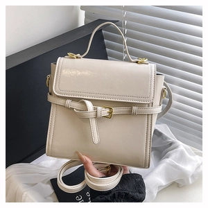 Close-up of cream white crossbody bag with glossy faux leather and golden hardware buckle