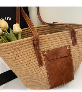 Detail of woven straw tote bag featuring brown leather pocket and white stitching accents