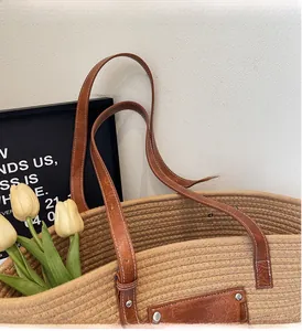 Detail of reinforced brown leather handles with white stitching on woven straw tote bag