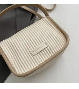 Detail of cream bucket bag featuring vertical pleated texture and brown leather trim