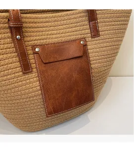 Detail of woven straw tote bag with brown leather pocket and metal rivet accents