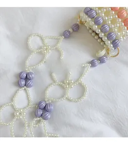 Détail d'un sac à main en perles blanches et violettes avec une bandoulière à fleurs