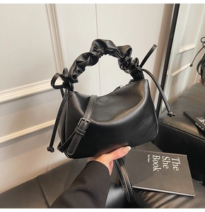 Detail of black soft leather handbag featuring unique pleated handle and brand lettering