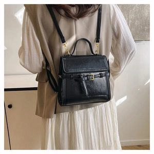 Macro detail of glossy black square bag featuring a top handle and gold metal buckles