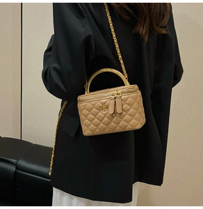 Detail view of beige quilted box bag with golden camellia floral ornament and chain strap
