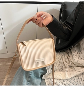 Detail of a beige pleated bucket bag with long crossbody strap and top handle design