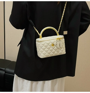 Rear view of model holding a white quilted box bag with golden metal handle and chain strap