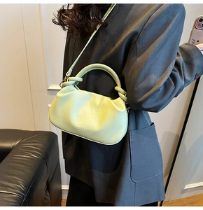 Pistachio green pleated handbag with round handle and shoulder strap worn with blazer
