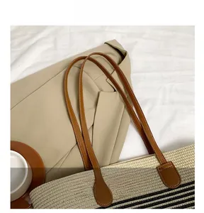 Detail of striped straw tote bag featuring brown leather handles and woven texture
