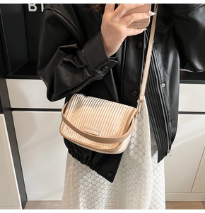 Detail of pleated beige crossbody bucket bag with elegant metal logo and soft leather texture