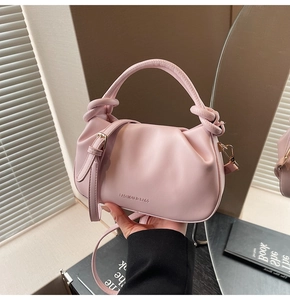 Close-up of pink ruched cloud handbag with knotted handle and gold metal hardware hooks