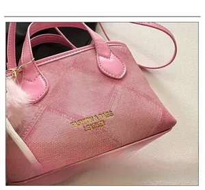 Detailed view of pink textured bucket bag with gold lettering and plush ball charm