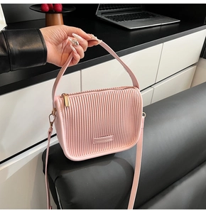 Detail of pink pleated bucket bag with metallic logo plate and adjustable shoulder strap