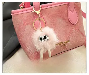 Detail showing the pink bucket bag with a cute plush charm and gold brand lettering