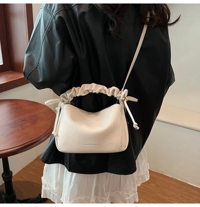 Detail of the pleated handle and drawstring bow on the beige ruched crossbody bag
