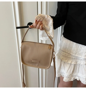 Detail of khaki pleated leather bucket bag featuring vertical folds and metal fashion label
