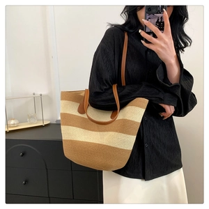 Detail of striped straw tote bag with brown leather handles worn by a model
