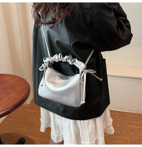 Silver metallic bag with ruched handle shown on shoulder in a minimalist indoor setting