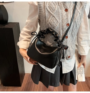 Detail of black pleated handle handbag with side bow ribbon decoration shown on shoulder