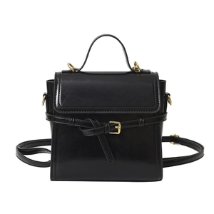 Glossy black mini handbag with gold buckle and top handle in a sleek structured design
